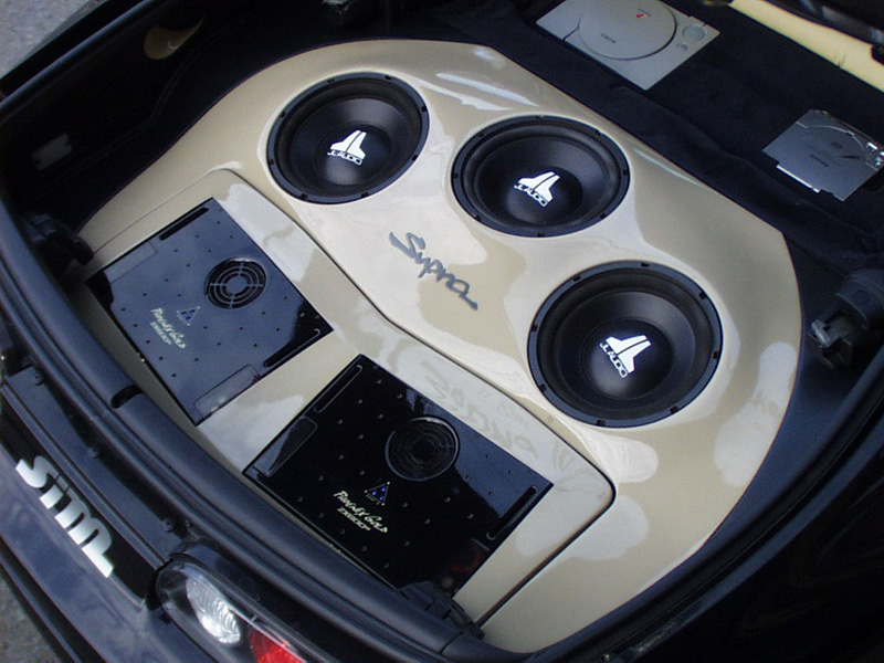 The original hatch floor was only raised slightly to accommodate series amounts of equipment and still fit the targa top. For regular (sound quality) listening, only the outside two of the three JL Audio 10W6 are being used. Each has its own 0.6 cu.ft. sealed enclosure with the center sub having a very small airtight steel enclosure around it. (See following picture). This steel enclosure has two airtight doors that can be opened electronically to allow all three subwoofers to play in one common enclosure. This is only used to achieve maximum SPL during competition. In this setting a Phoenix Gold Bass Qube is engaged as well that is precisely tuned to the resonant frequency of all three woofers in a single enclosure. All this is documented with a small B/W camera inside the enclosure showing the mechanics and how the doors open and close.